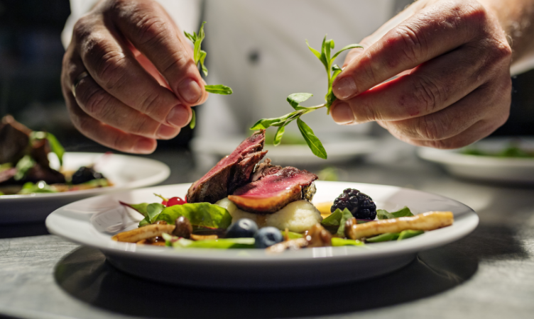 tendências gastronômicas: mãos de um chefe de cozinha finalizando um prato de comida