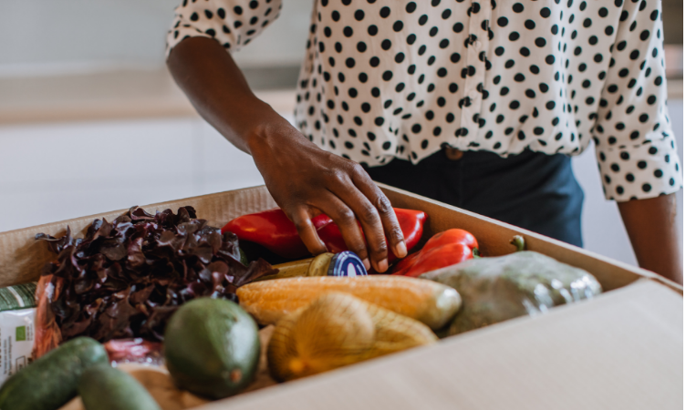 mão de uma mulher negra tocando em frutas e legumes dentro de uma caixa - mercado de orgânicos