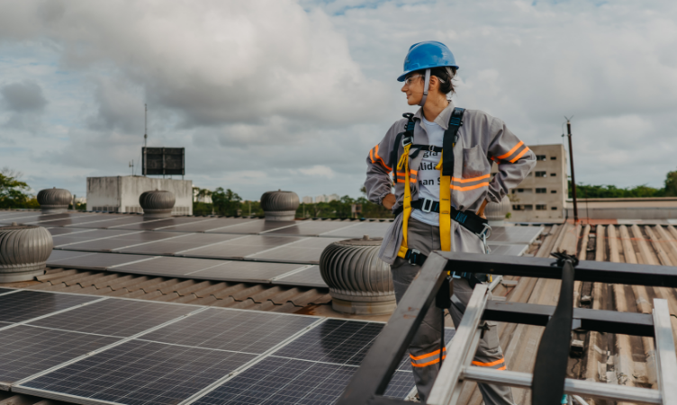 mercado livre de energia - Mulher usando equipamentos de segurança em cima de uma telhado com placas de energia fotovoltaica