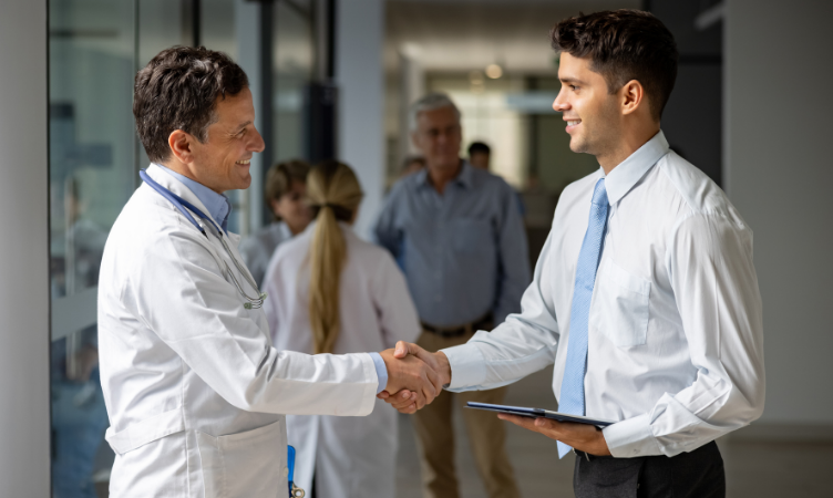 Imagem destaque do blogpost do Sebrae RS sobre vendas na área da saúde. Nele um homem de terno apertando mão de um médico dentro do corredor de um hospital.
