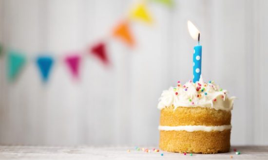 bolinho recheado com uma vela de aniversário acesa com enfeites de festa ao fundo - 15 anos do MEI