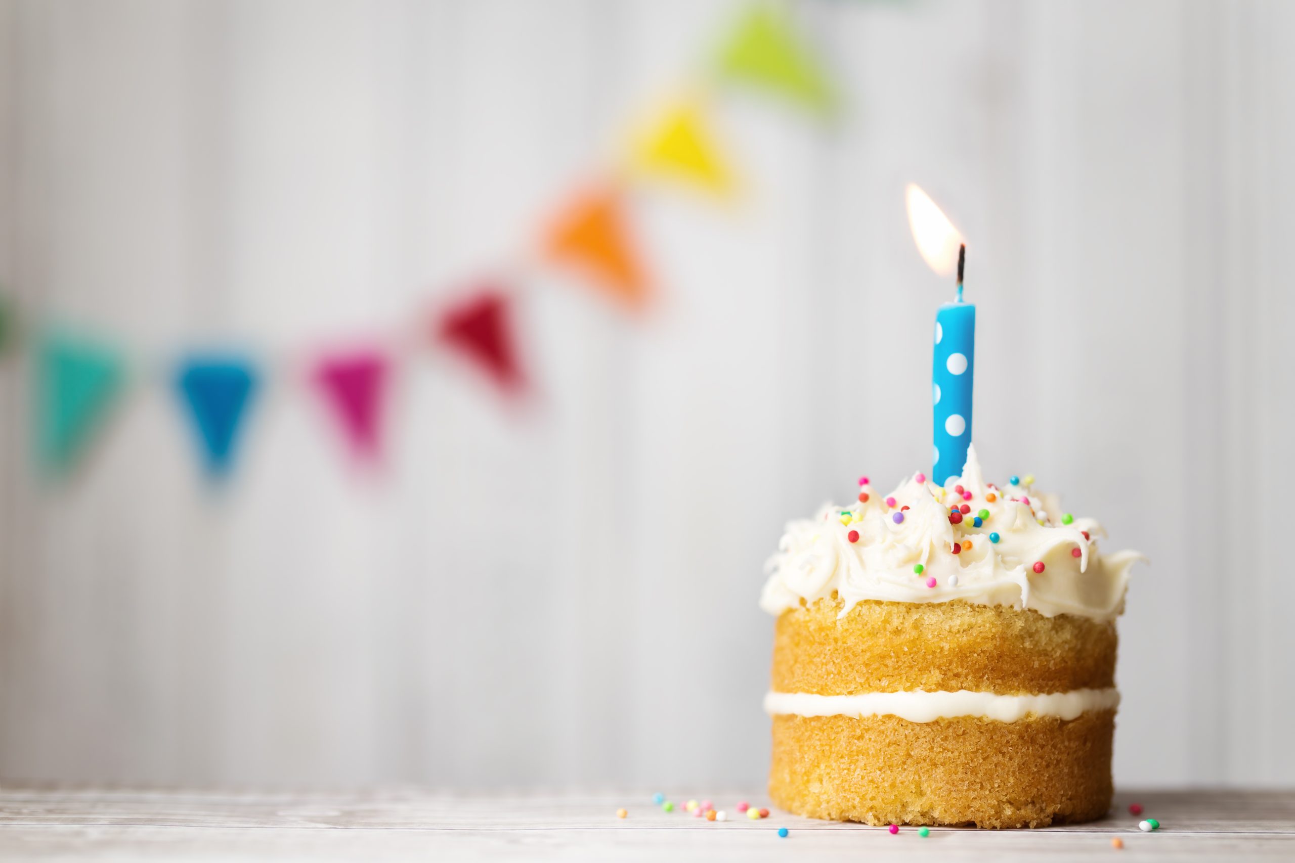 bolinho recheado com uma vela de aniversário acesa com enfeites de festa ao fundo - 15 anos do MEI