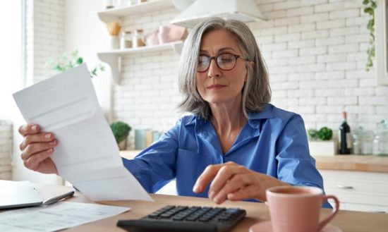 Imagem do postblog Como emitir a parcela do parcelamento do MEI. Mulher segurando folha de papel e usando uma calculadora.