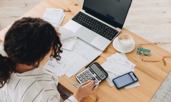 mulher fazendo cálculos com papéis e notebook em cima de uma mesa - post Exclusão do Simples Nacional