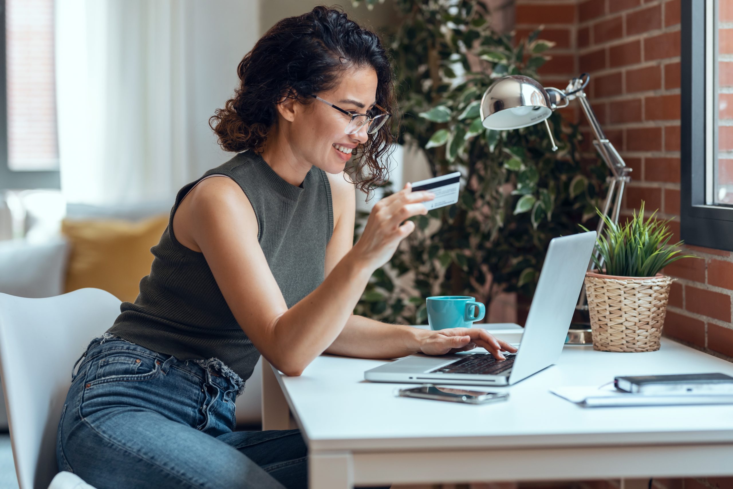 Imagem de destaque do post Cartão MEI: benefícios exclusivos para Microempreendedores Individuais. A imagem contém uma mulher segurando um cartão de crédito em frente a um notebook