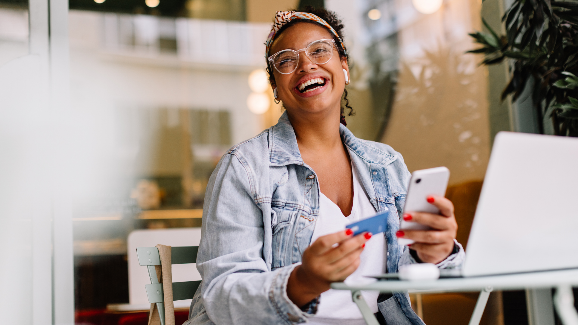 blogpost canal de compra - mulher sorrindo em frente ao notebook com um celular e um cartão de comprar na mão.