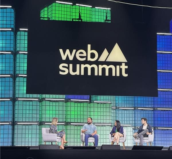 web summit rio 2025 - imagem do telão do evento, com fundo azul e verde, e palestrantes sentados ao palco.