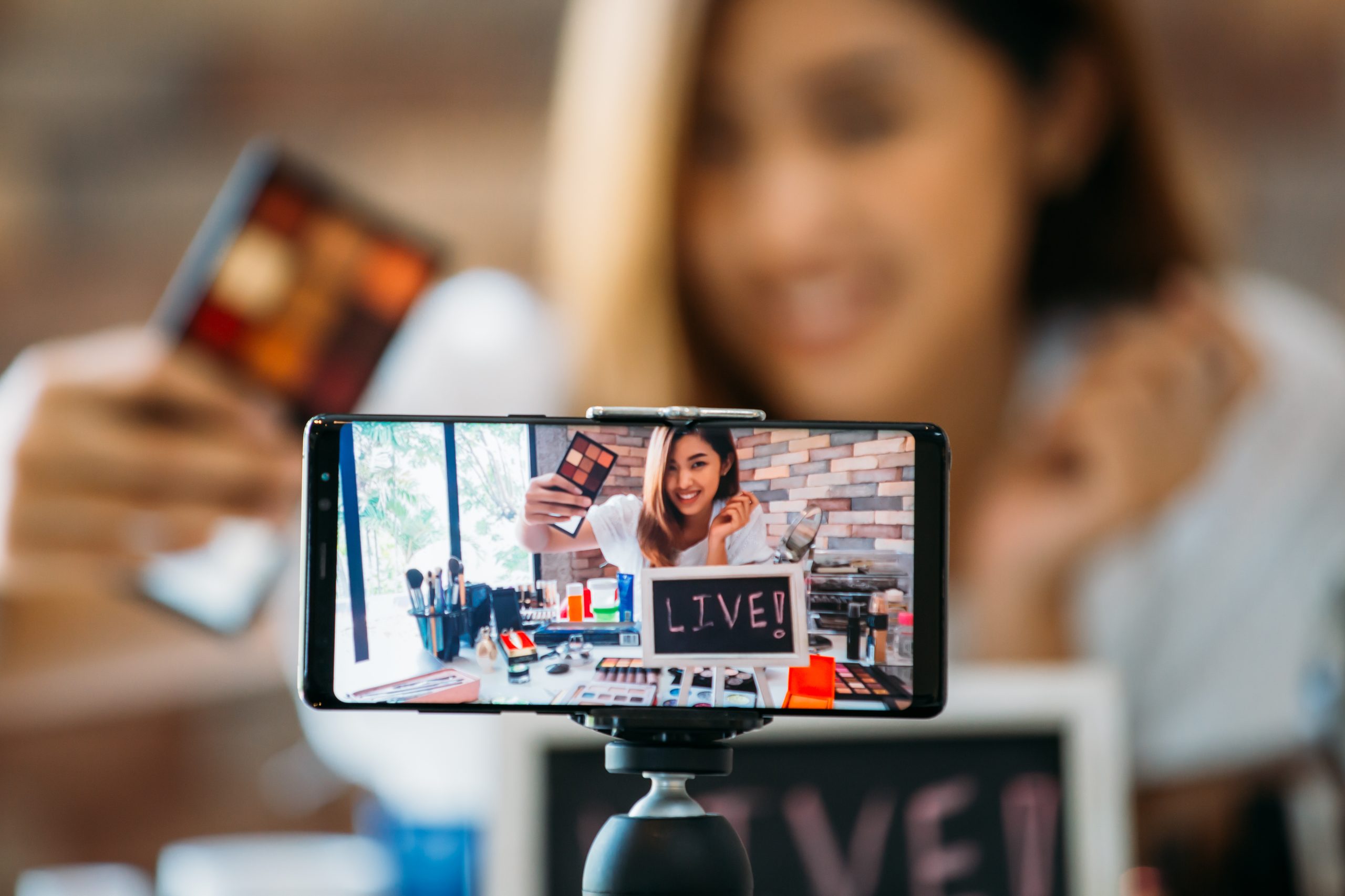 como criar conteúdo - Imagem de destaque do post Presença digital sem complicação como usar tua rotina para criar conteúdo. A imagem contém um celular gravando uma live de uma mulher mostrando produtos de beleza.