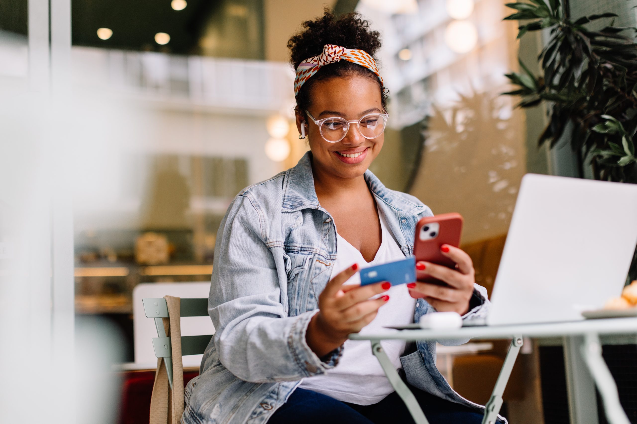 Imagem do post MEI: agora o pagamento do DAS pode ser feito com cartão de crédito. A imagem contém uma mulher com celular e um cartão de crédito nas mãos. Ela está em uma mesa com notebook.
