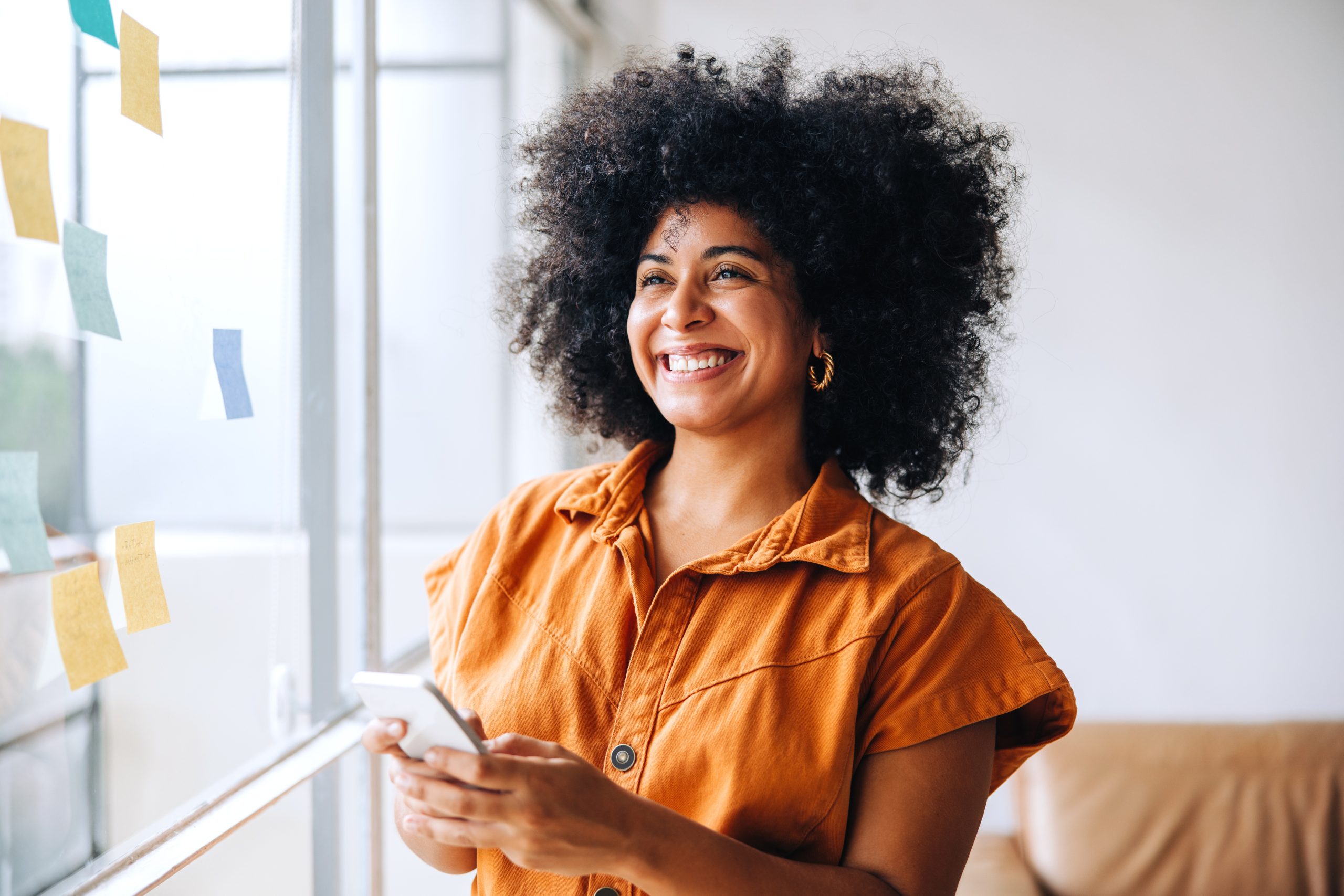 imagem blog A economia dos criadores não é só para influencer. Mulher sorrindo com um celular nas mãos, em um ambiente de trabalho com anotações ao fundo.