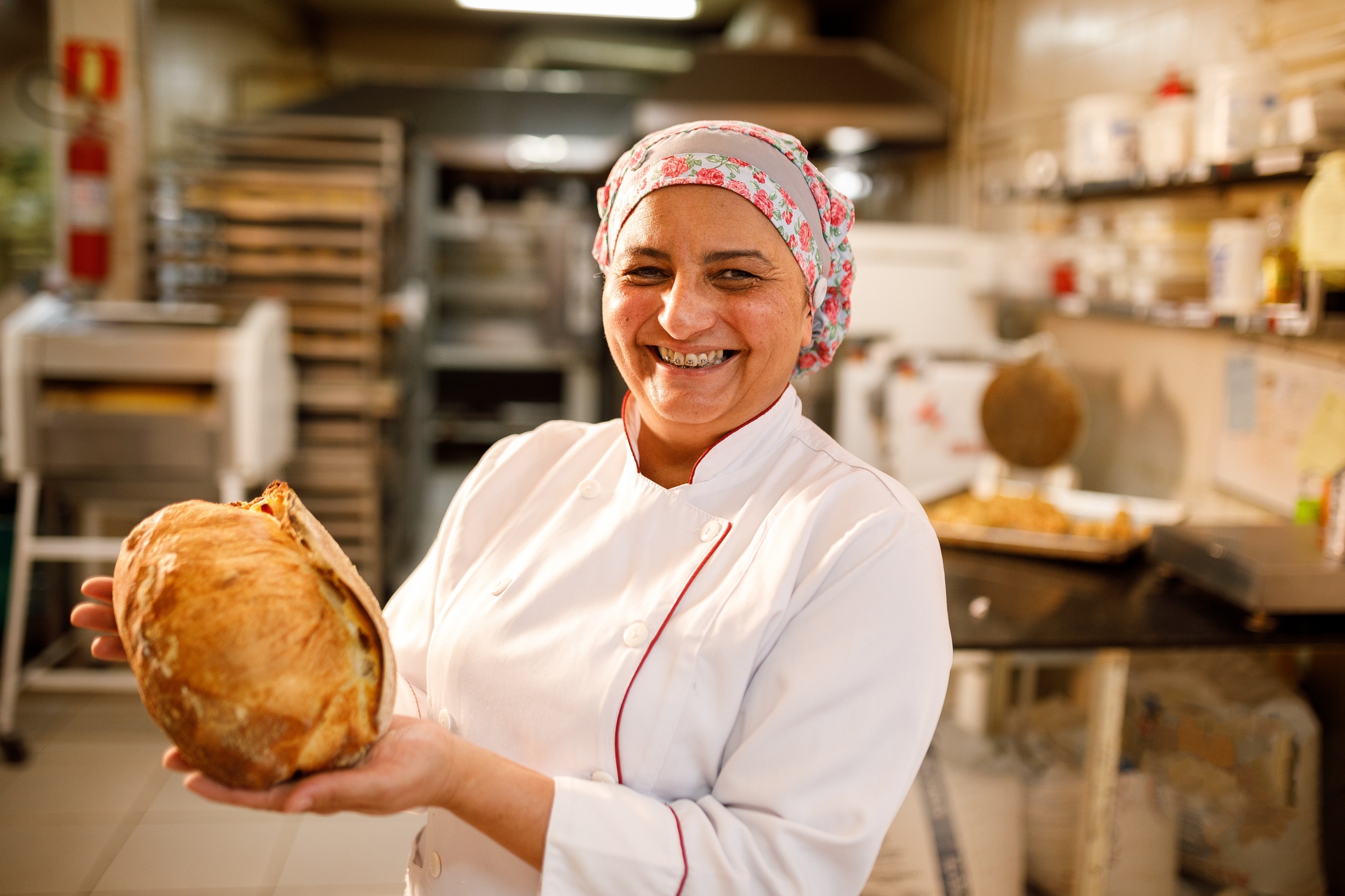 imagem blogpost Alimentos artesanais do RS. Mulher sorrindo e segurando um pão em sua padaria. 