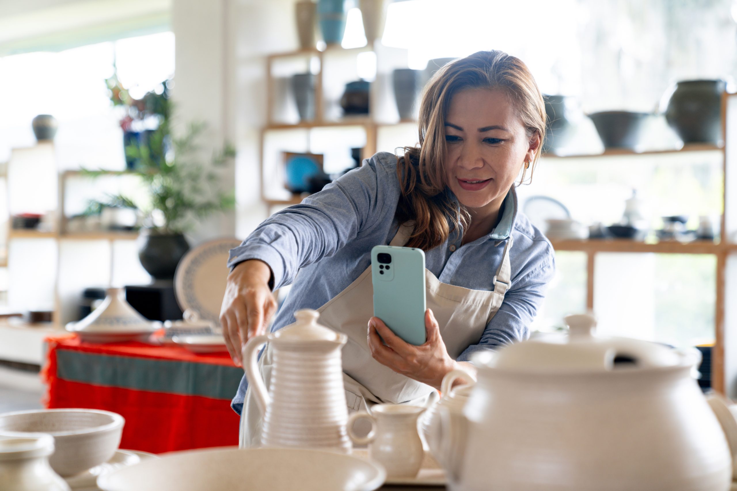 imagem blog A economia dos criadores não é só para influencer. Mulher trabalhando com peças de cerâmica enquanto utiliza o celular.