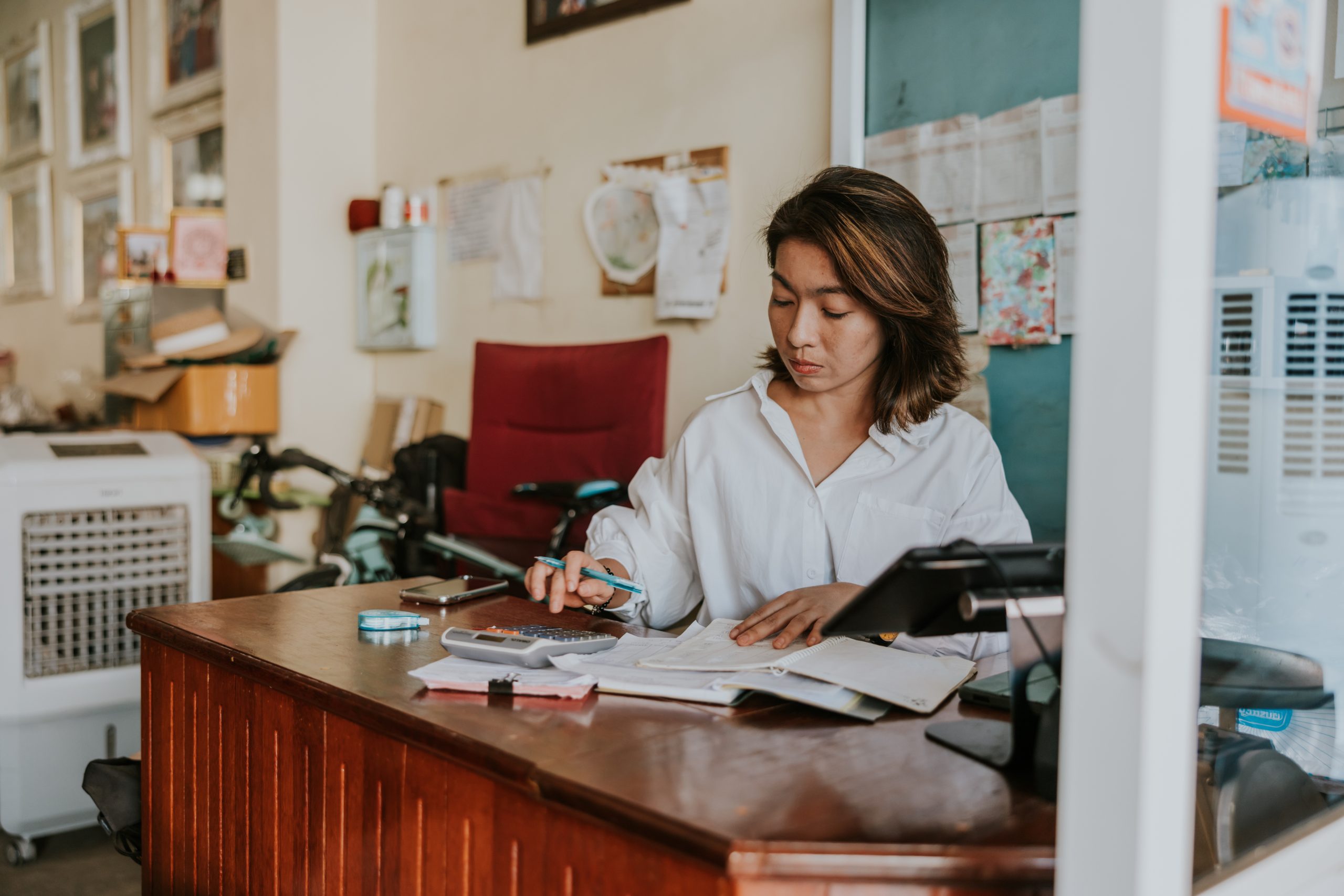 imagem blogpost Capital de giro. Mulher analisando documentos e utilizando uma calculadora em um ambiente comercial.